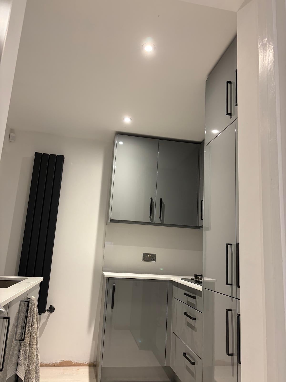 Modern fitted kitchen area with grey gloss wall and base units featuring black handles, white worktop, and integrated appliances