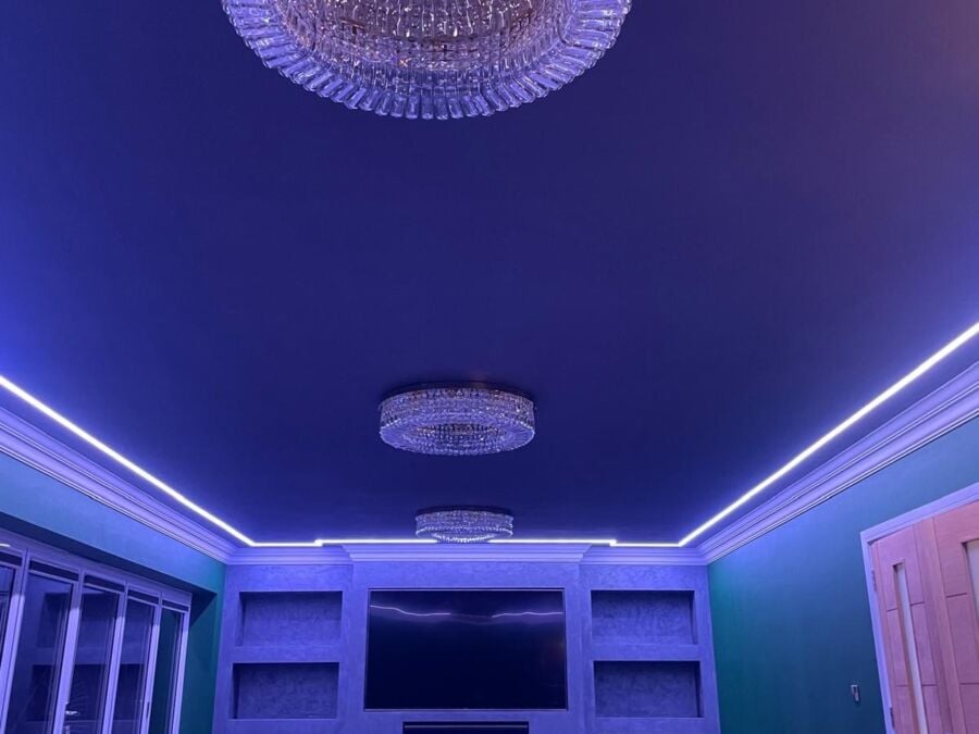 Large open plan living space with decorative ceiling featuring three crystal chandeliers and purple LED perimeter lighting in recessed coving