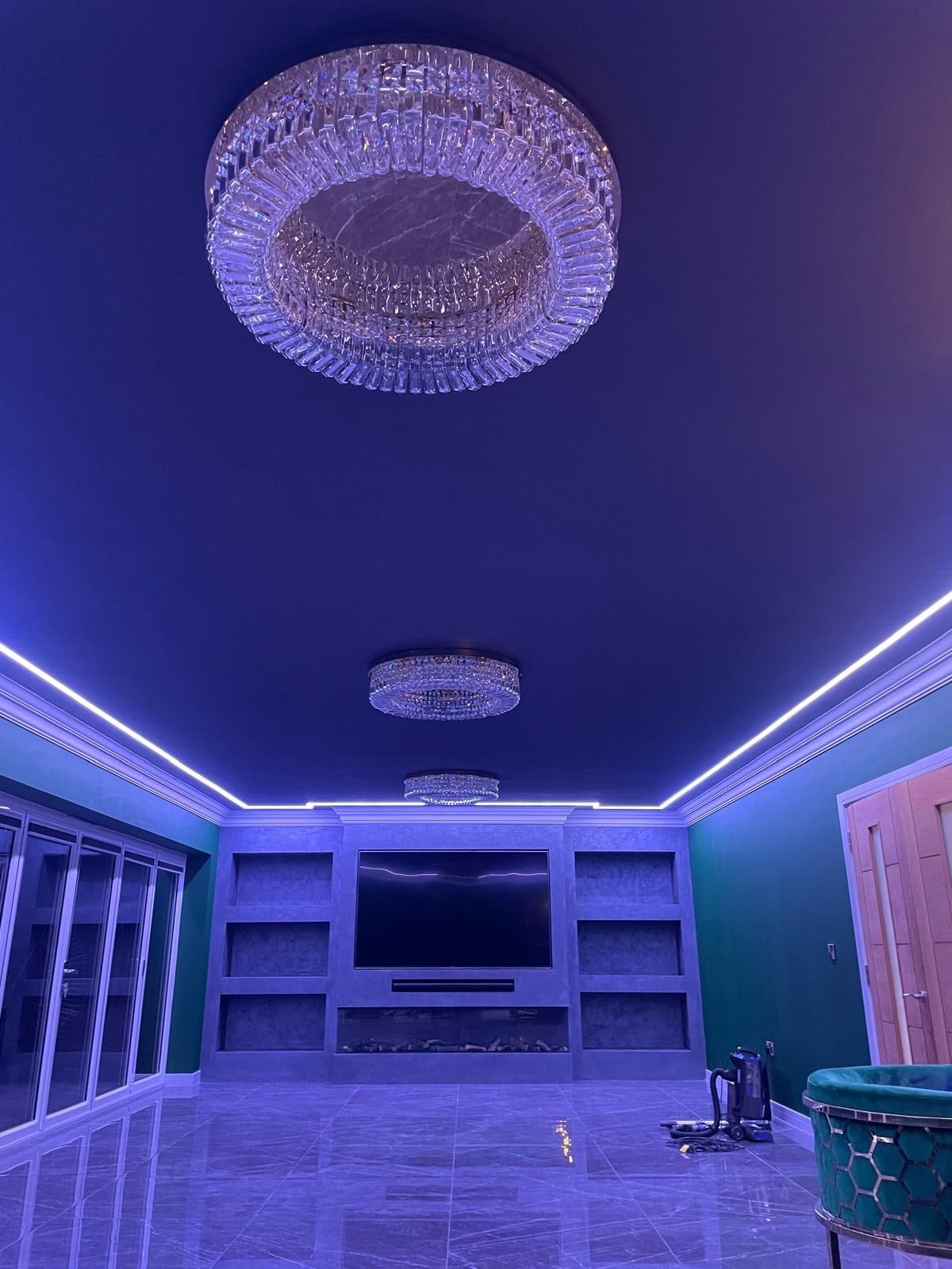 Large open plan living space with decorative ceiling featuring three crystal chandeliers and purple LED perimeter lighting in recessed coving