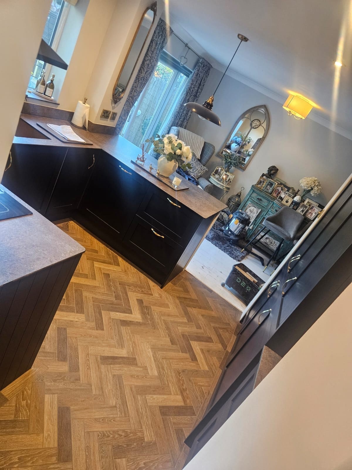 Open plan kitchen and dining area featuring herringbone parquet flooring in natural oak, black gloss handleless base units with dark worktops
