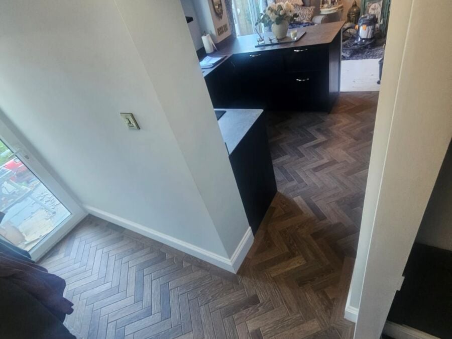 View from top of stairs showing herringbone pattern laminate flooring in grey tones throughout a hallway and landing area