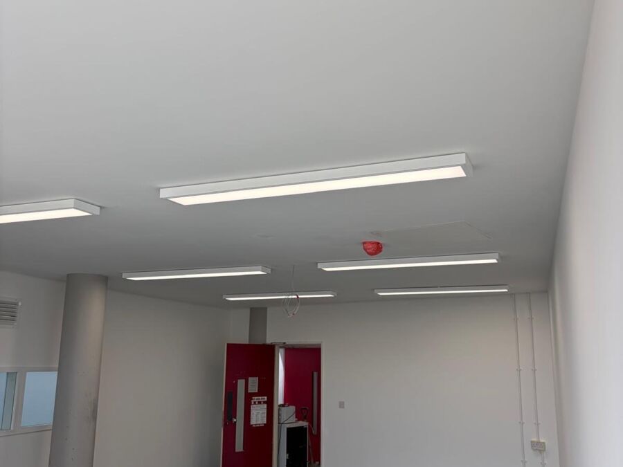 Commercial office space with white walls, dark carpet flooring and modern LED panel light fittings installed across the ceiling