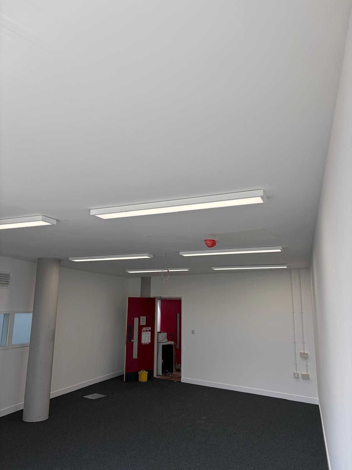 Commercial office space with white walls, dark carpet flooring and modern LED panel light fittings installed across the ceiling