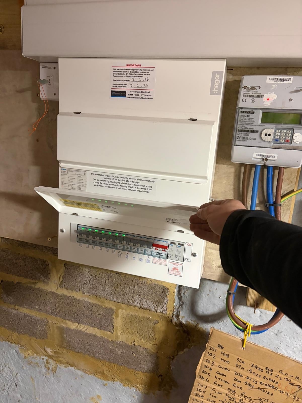 An electrician inspects an open consumer unit and fuse box installation mounted on an interior wall, with visible circuit breakers, electrical wiring