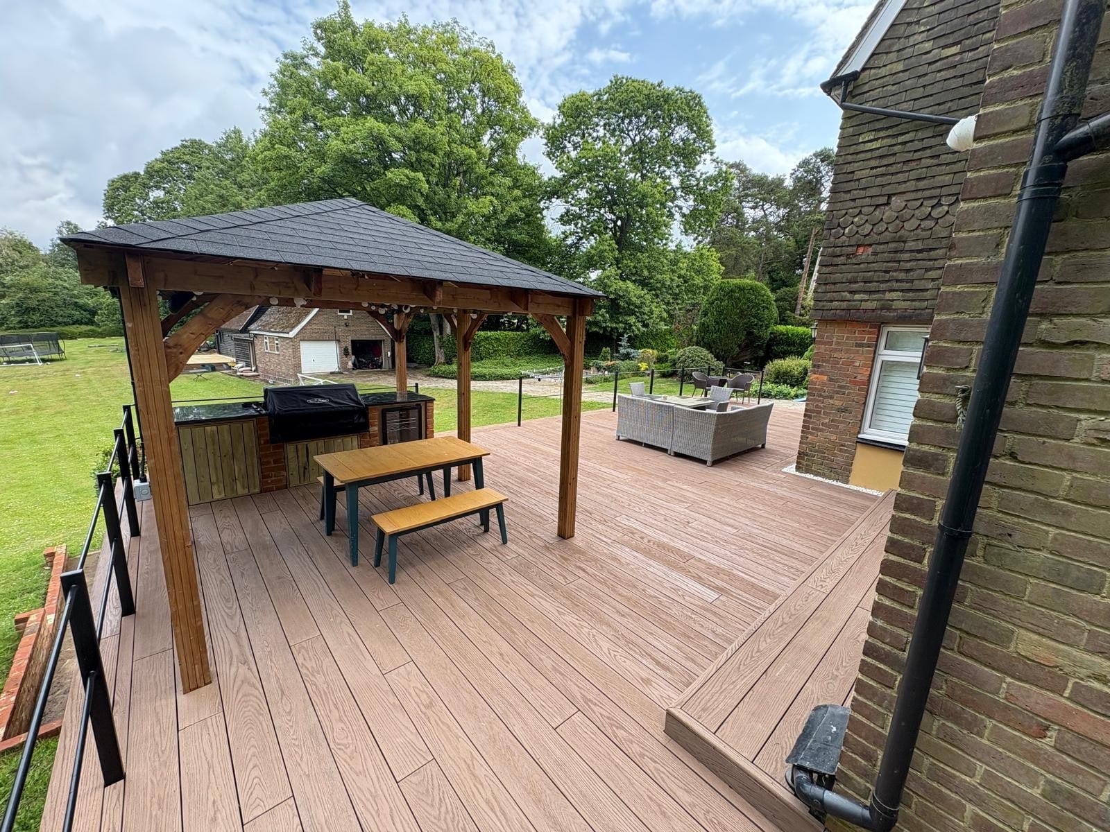 Composite decking installation in wood effect finish featuring timber framed gazebo with slate roof, metal railings