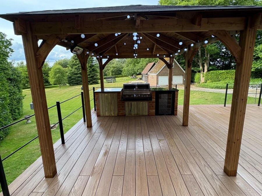 Outdoor timber pergola with pitched roof covering a wooden deck area, featuring an integrated outdoor kitchen unit with barbecue and storage