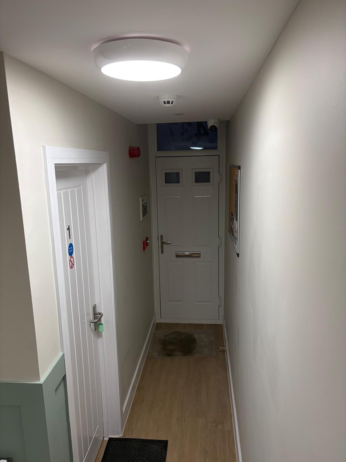 Residential entrance hallway featuring white painted walls, ceiling mounted flush light fitting, smoke detector, and laminate flooring
