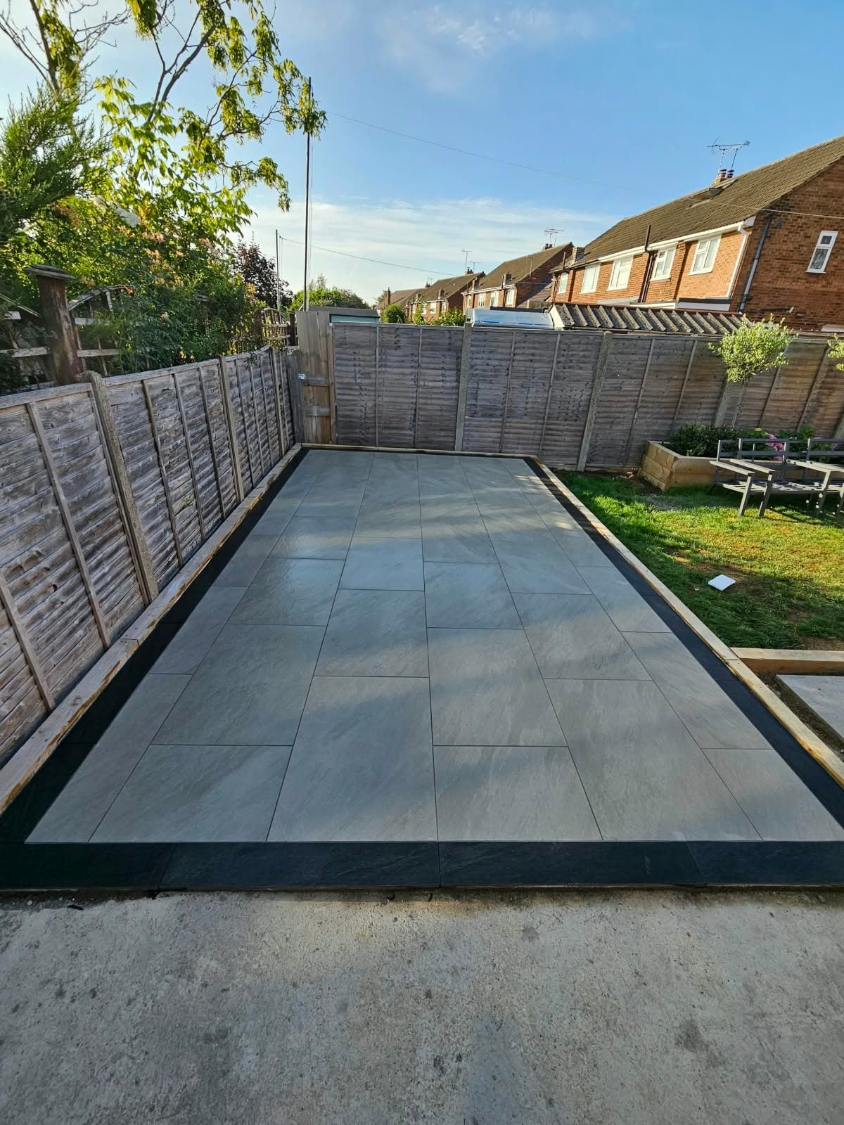 Newly laid patio featuring large format grey porcelain tiles with timber edging in a residential garden