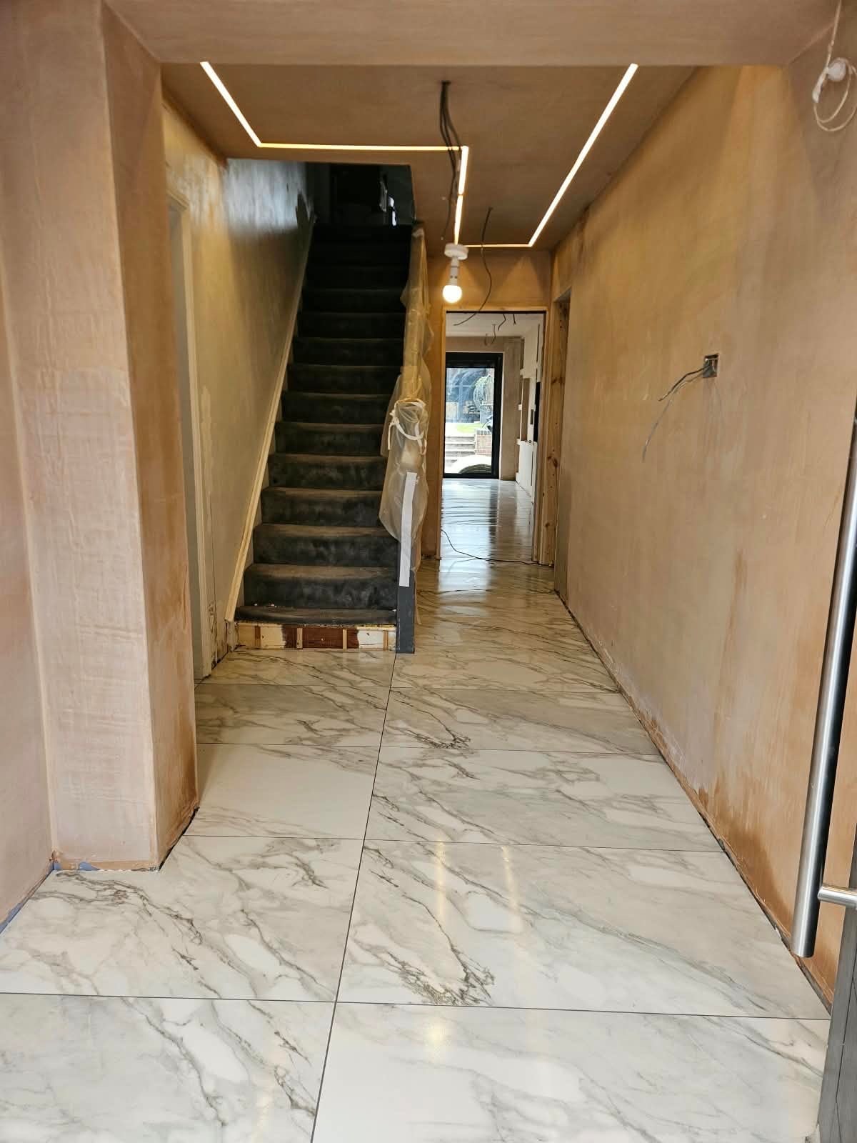 Residential hallway and staircase during renovation showing marble effect floor tiles, plastered walls awaiting decoration