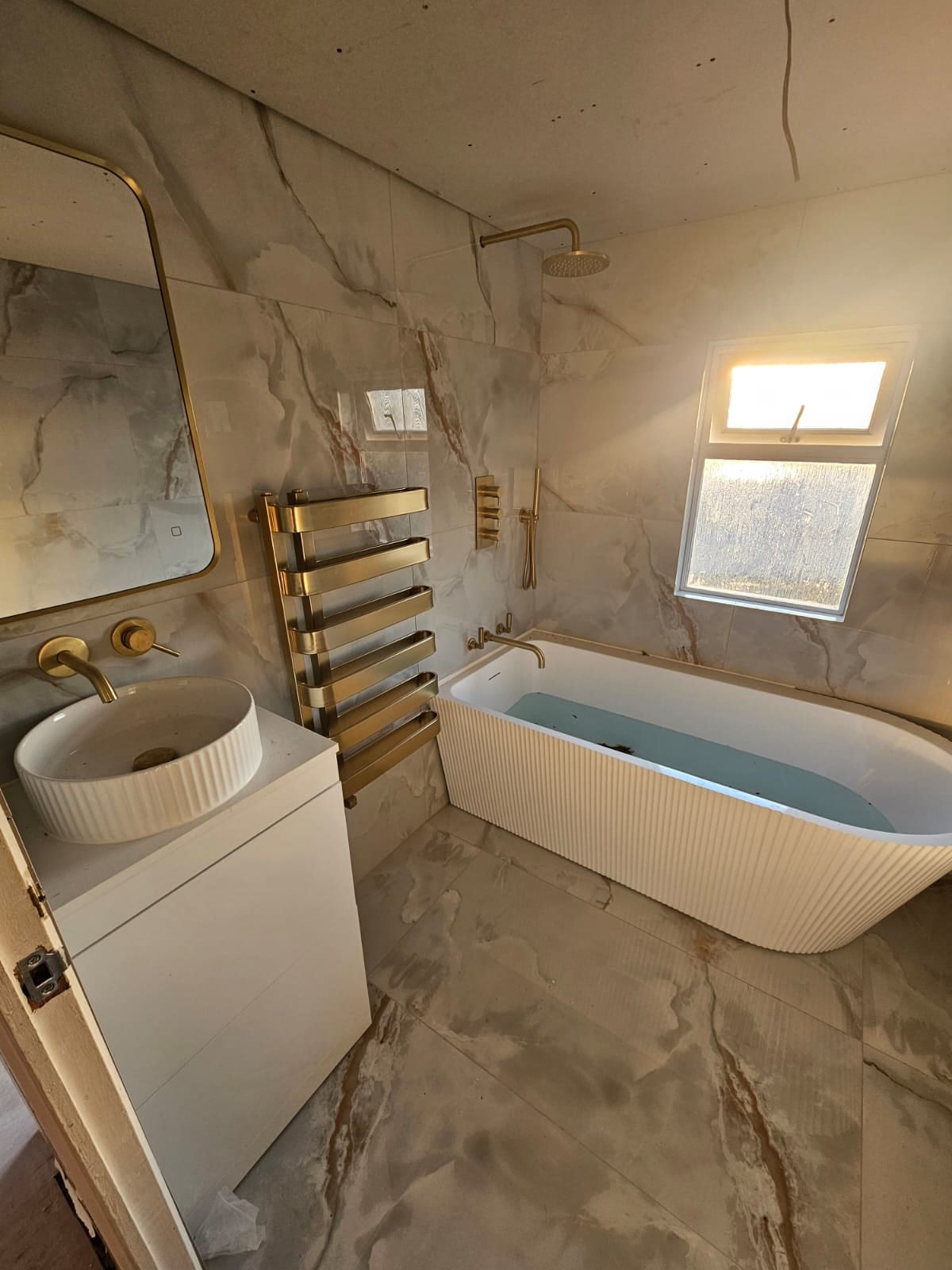 Luxury bathroom with black marble effect porcelain tiles and backlit mirror, finished by Brooks Contractors