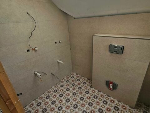 Loft bathroom installation in progress with beige wall tiles fitted throughout and decorative patterned floor tiles