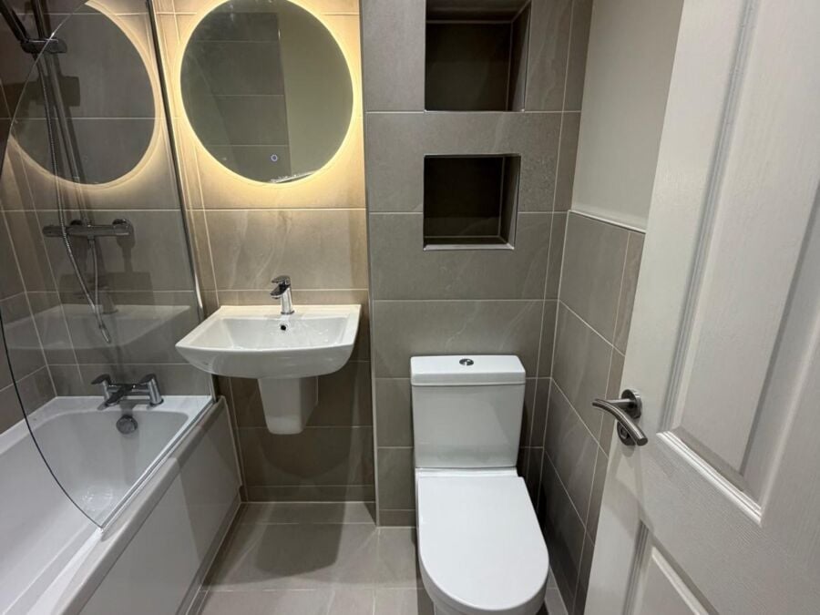 Bathroom with grey tiles, round backlit mirror and recessed shelves