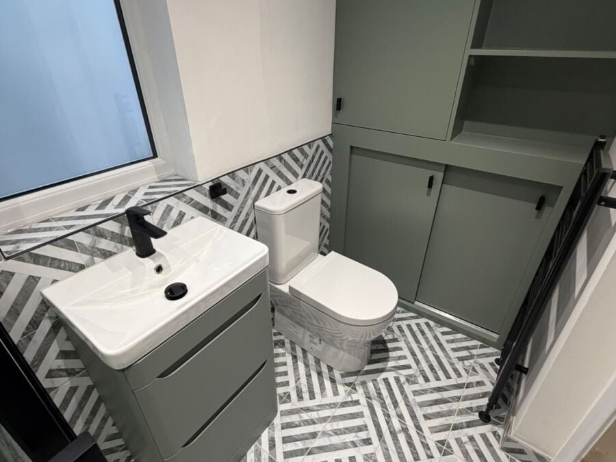 Bathroom with herringbone floor tiles, sage green vanity and storage
