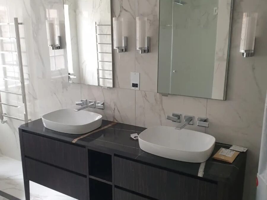 Modern bathroom installation featuring a dark wood double vanity unit with white oval countertop basins, marble effect wall tiles