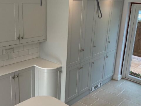 Fitted shaker kitchen in pale grey with tall larder units, a curved end cabinet and tiled floor