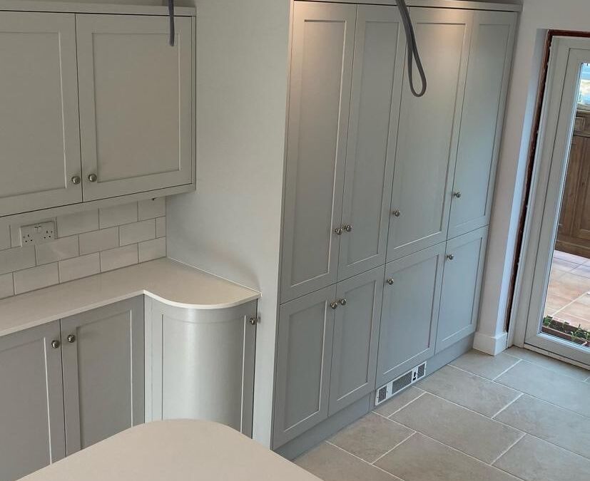 Fitted shaker kitchen in pale grey with tall larder units, a curved end cabinet and tiled floor
