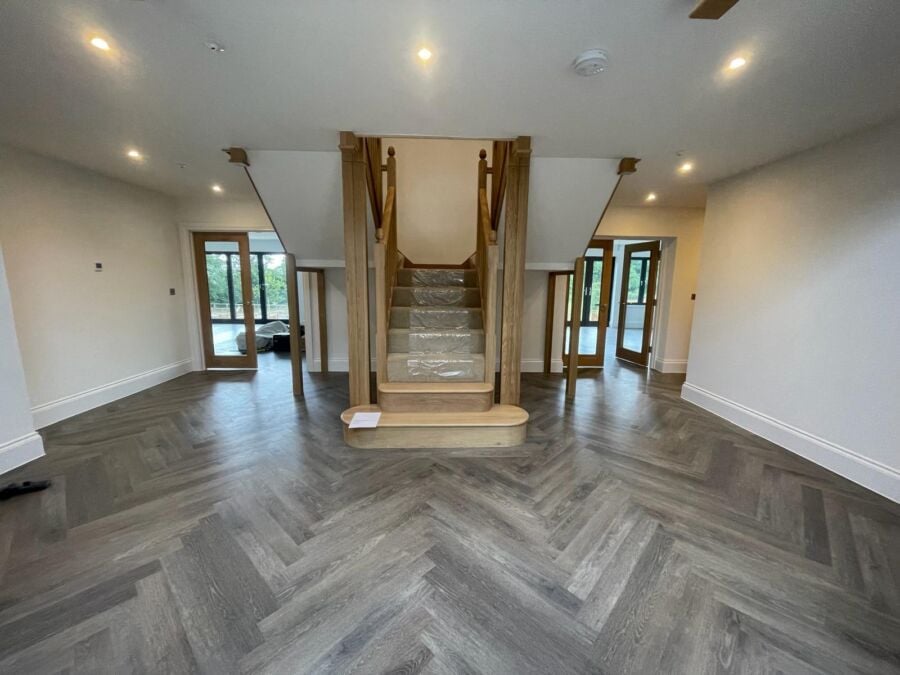 Open plan hallway with grey herringbone flooring and an oak staircase
