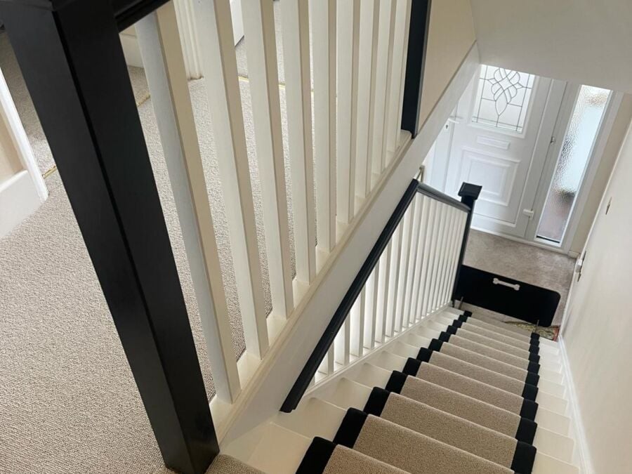 Staircase with a black handrail, white spindles and a carpet runner