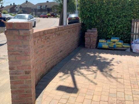 New red brick boundary wall with a capped pier beside a block paved drive