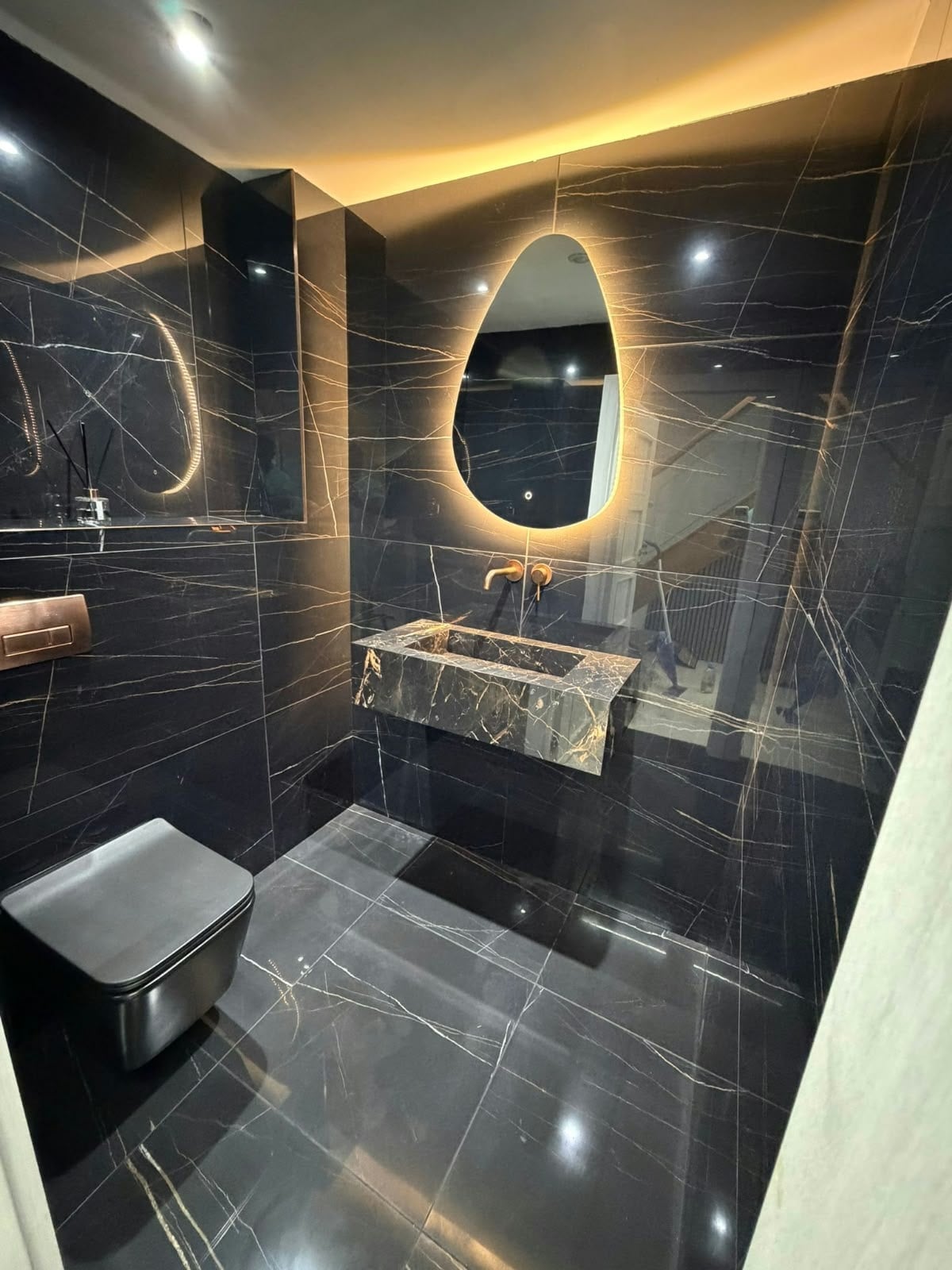 Modern bathroom featuring large format black marble effect porcelain tiles on walls and floor, with a floating marble vanity basin