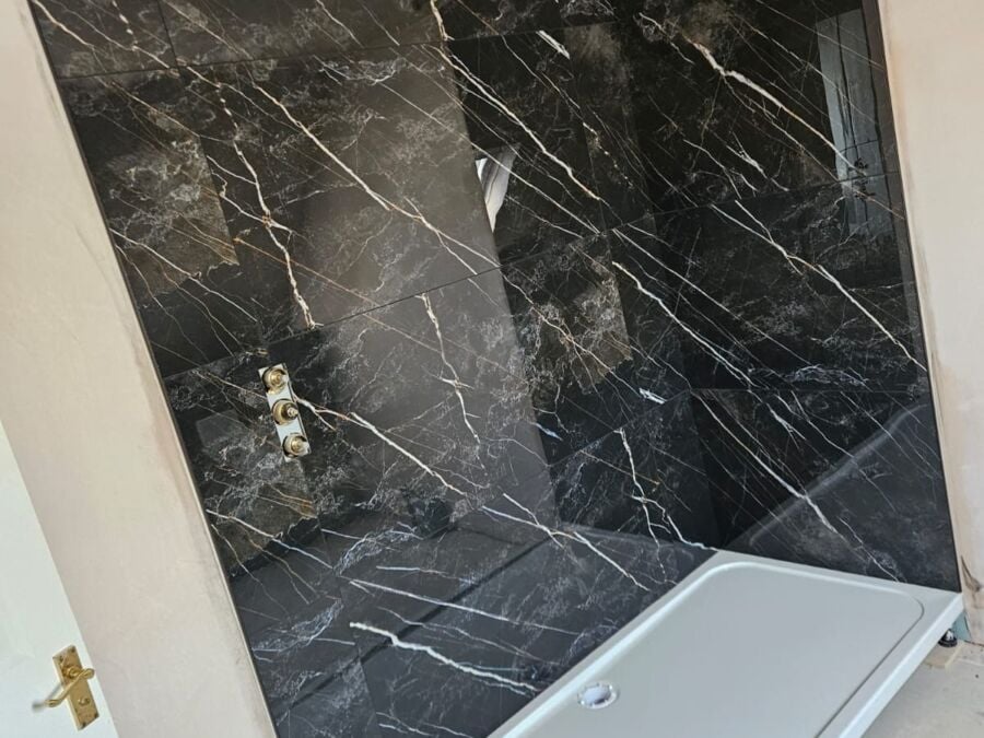 Black marble effect wall panelling installed in a bathroom, featuring white veining detail and exposed shower valve fittings