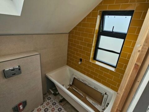 Loft bathroom conversion featuring mustard yellow metro tiles on the sloped ceiling wall, beige tiles on lower walls