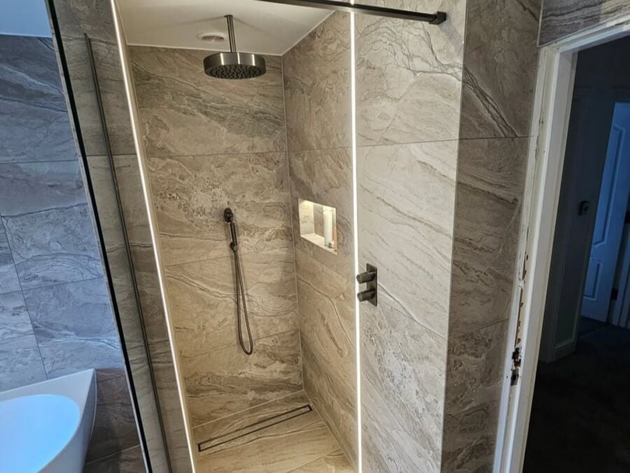 Modern walk in shower enclosure featuring large format grey marble effect tiles with veined pattern, frameless glass screen with black fittings